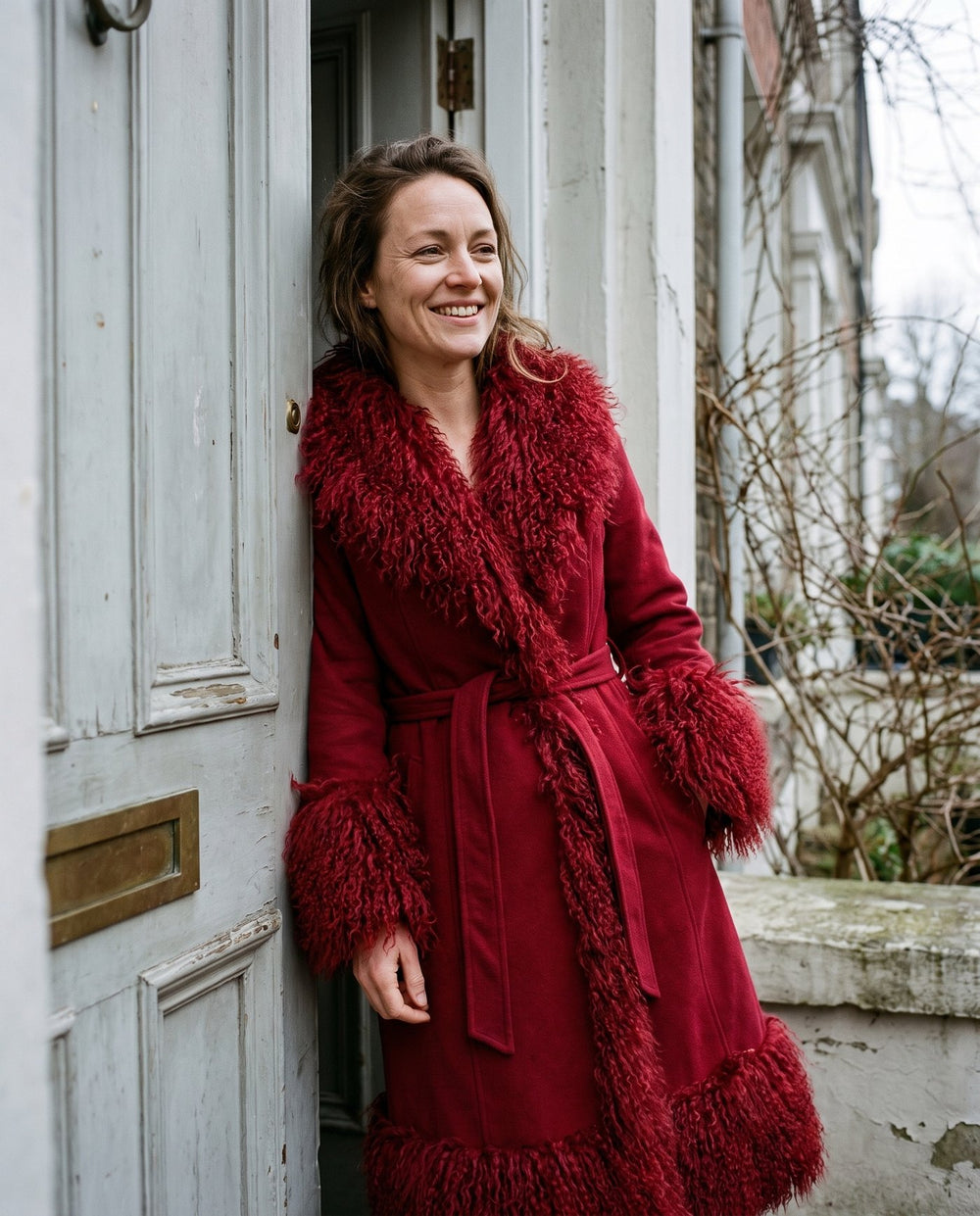 The Ember coat worn belted in a doorway, showing the faux fur collar and cuffs, Fox & Ocean