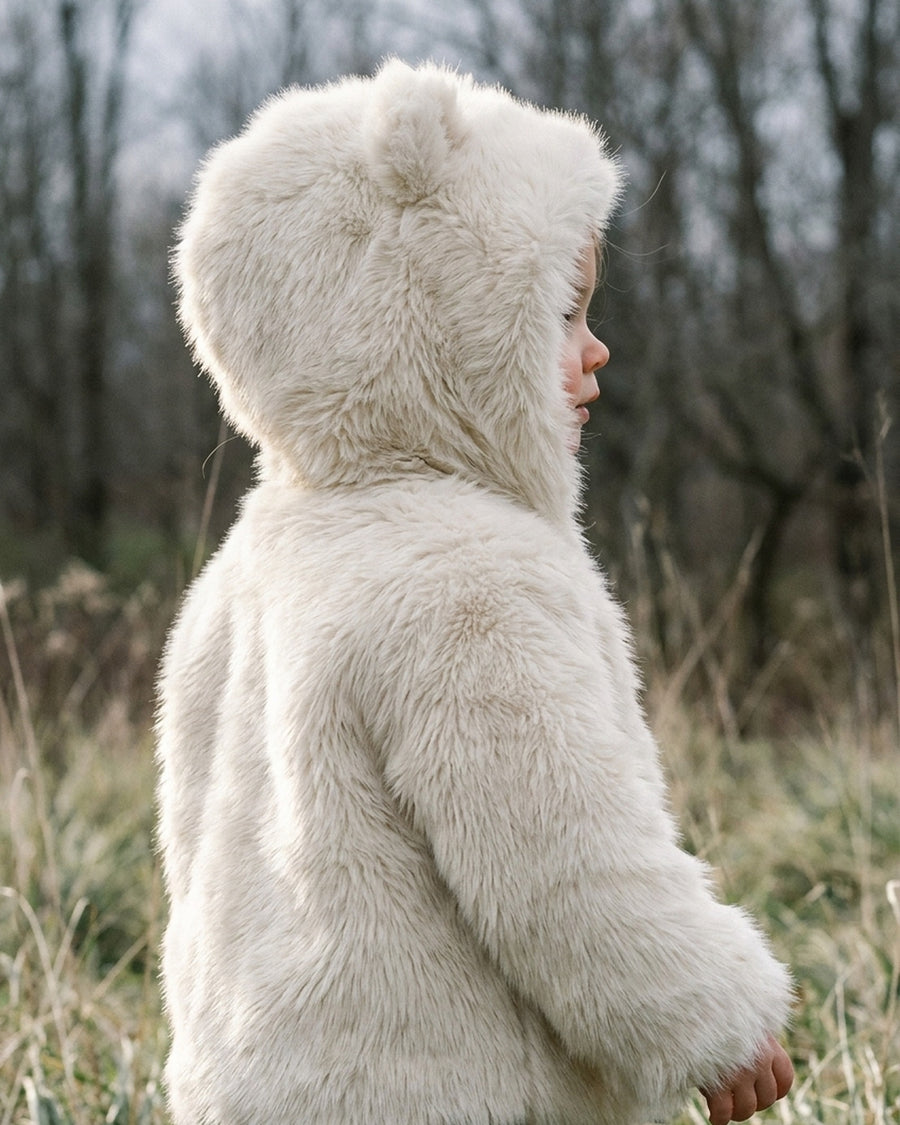 Close view of a child wearing the Snowfall Little Bear coat with the hood up, both rounded bear ears visible, long fur pile catching the light